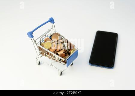 Shopping cart full of coins with a smart phone.Money and financial concept.Phone with black screen mockup banner template.E-commerce ,business marketi Stock Photo