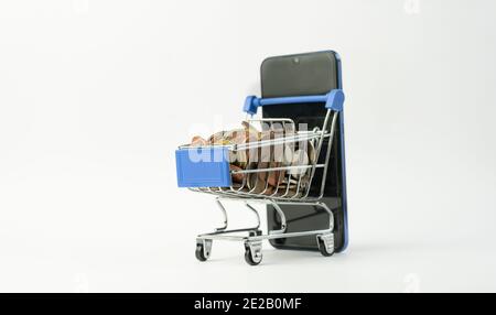 Shopping cart full of coins with a smart phone.Money and financial. E-commerce business marketing online shopping ,mini supermarket trolley on isolate Stock Photo