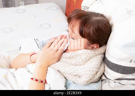 a young pretty girl is sick at home in bed and blows her nose in a handkerchief Stock Photo