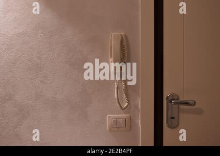 A white wall with an intercom hanging on the wall, a light-on button and an armored door (Pesaro, Italy, Europe) Stock Photo