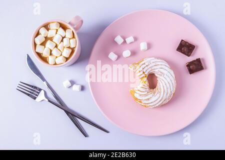 Top view still life of a bitten cake on a pink plate, cutlery and a cup of cocoa with marshmallows. Selective focus, horizontal orientation. Stock Photo