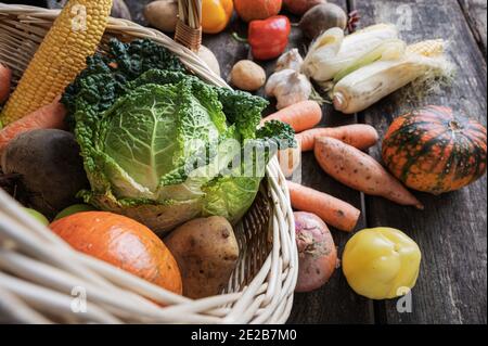 Wicker basket full of various colorful vegetables scattering on rustic wooden boards. Stock Photo