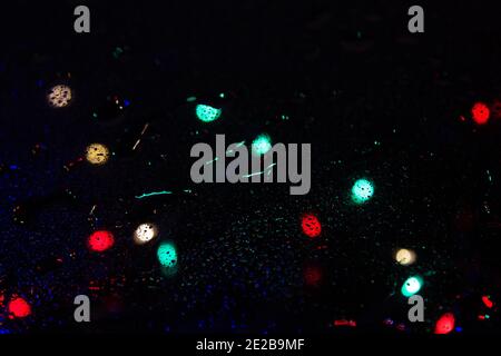 Colorful bokeh lights on a dark background behind the raindrops on the glass texture Stock Photo