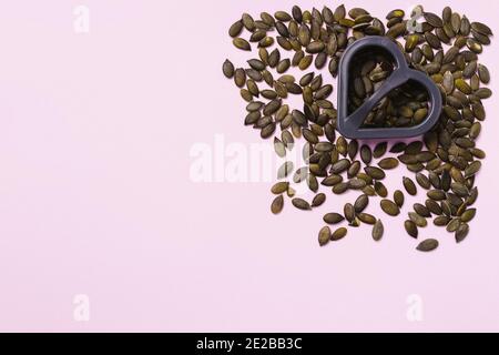 Pink background. Pumpkin seeds in the right corner and a heart-shaped cookie cutter. Empty space for advertising. Stock Photo