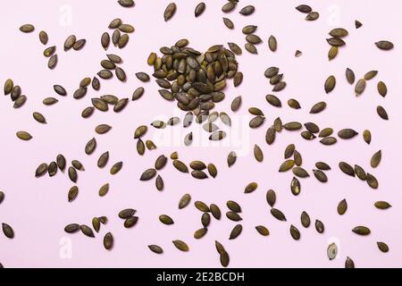 Pumpkin seeds are painted on a pink background in the shape of a heart. Stock Photo