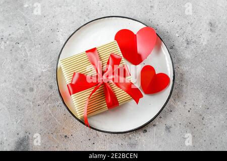 Valentine's Day Table Setting. Plate with Gift box and two red hearts. Flat lay, top view Stock Photo