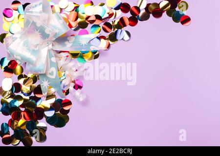 Lined with colored confetti and a gift bow on a purple background with blank advertising space. Stock Photo