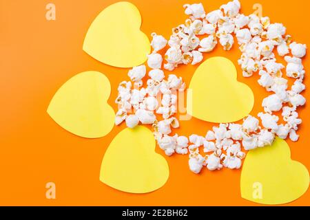 Scattered popcorn and illuminating hearts on orange background. Valentine's Day. Stock Photo