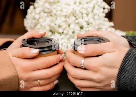 male and female hands hold two brown glasses of coffee, next to a bouquet of gypsophila flowers Stock Photo