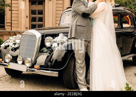 newlyweds hug and dance near the car, the bride and groom hold hands near the retro car Stock Photo