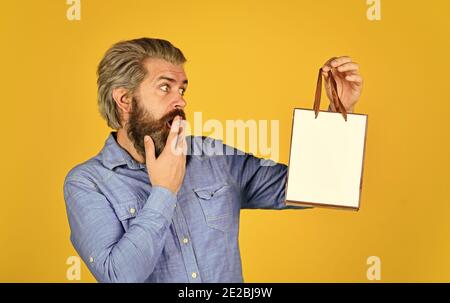 bearded man hold paper bag. presents. delighted man shopping online. surprised hipster making purchases at electronics store. Positive man enjoying shopping. Own business. Choosing the best. Stock Photo