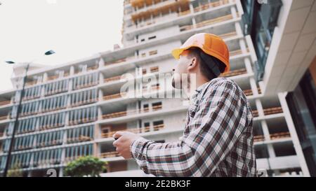 Entrepreneur on construction site using smartphone, checking work plans. Civil engineer or architect with hardhat checking schedule on smart phone. En Stock Photo