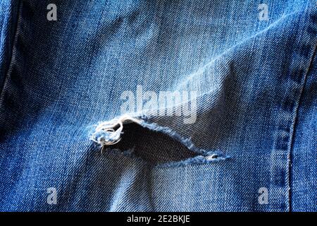 Ripped blue jeans torn texture background. Hole and Threads on Denim Jeans Stock Photo