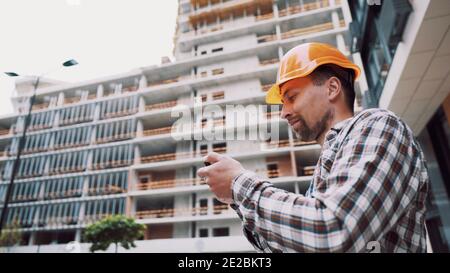 Entrepreneur on construction site using smartphone, checking work plans. Civil engineer or architect with hardhat checking schedule on smart phone. En Stock Photo