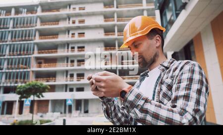 Entrepreneur on construction site using smartphone, checking work plans. Civil engineer or architect with hardhat checking schedule on smart phone. En Stock Photo