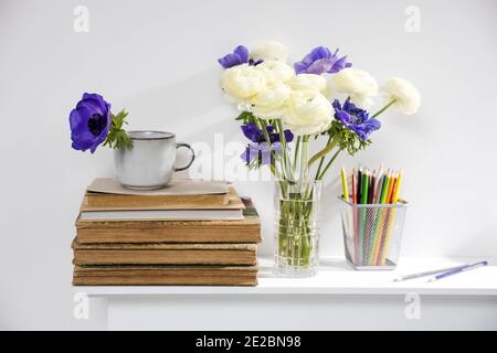 One blue anemone in a cup in the style of the seventies on the table with books as an interior decoration. Pencil holders with pencils and a vase of w Stock Photo