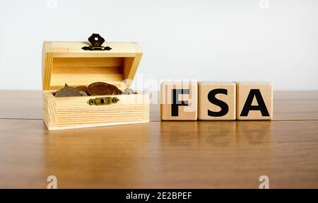 FSA symbol. Concept word 'FSA, flexible spending account' on cubes on a beautiful wooden table, small chest with coins. Beautiful white background. Bu Stock Photo
