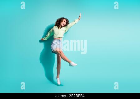 Full length body size photo of brunette girl dancing jumping keeping hand up singing isolated on vibrant teal color background Stock Photo