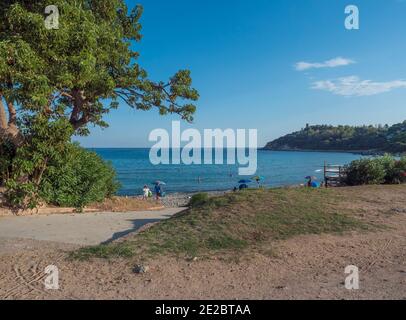 View of sand beach Porto Frailis with group of relaxing people, green trees. Summer blue sky and sea background. Arbatax, Tortoli, Sardinia, Italy. Stock Photo