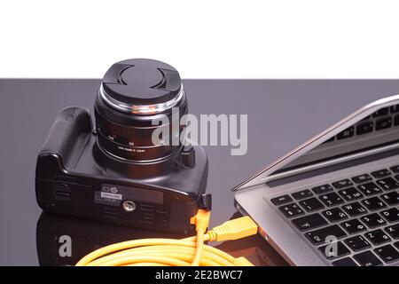 Digital photo camera connected to laptop with orange rolled cable. Stock Photo