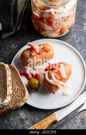 Pickled sausages with onion and red pepper. Marinated food on plate. Stock Photo