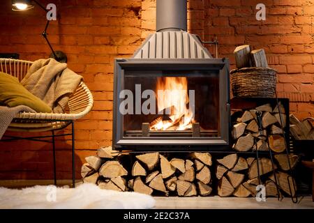 Cozy fireplace with firewood in the loft style home interior with brick wall background, burning fire in the fireplace, house coziness in winter Stock Photo