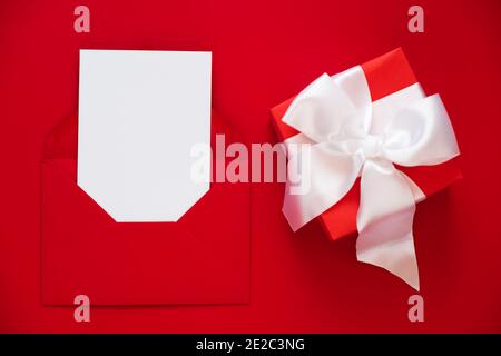 Mockup of greeting card in envelope and present on red background. Happy Valentines or Mothers Day. Top view with copy space Stock Photo