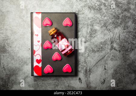 Image of a red love potion and pink heart shaped sweets on a gray gift box on a  concrete textured surface Stock Photo