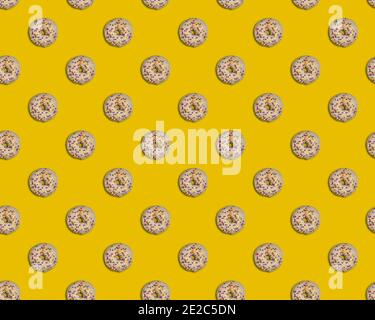 Seamless pattern with beautiful round doughnuts glazed with white chocolate and colorful yellow, purple, pink and white decor on bright yellow backgro Stock Photo