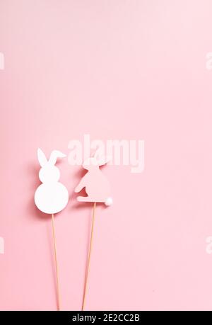 Easter vertical composition with traditional decor. Two rabbit decorative figures on wooden sticks on soft pink background. Stock Photo