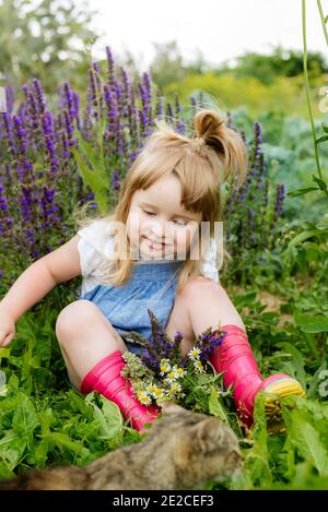 Happy little child with cat. Girl playing with pet outdoors on the garden. Summer nature Stock Photo