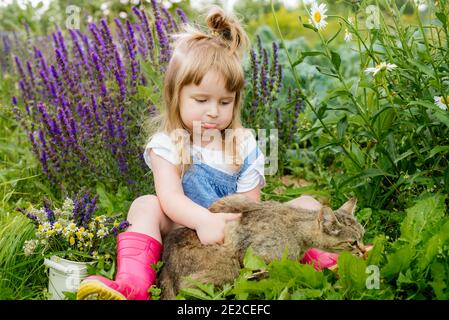 Happy little child with red cat. Girl playing with pet outdoors on the garden. Summer nature Stock Photo