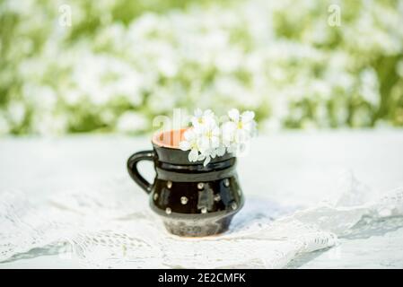 village and vintage, a gentle cozy morning, flowers.Black clay mug, sunny summer, wildflowers in a vase on a lace knitted tablecloth, lace. Stock Photo
