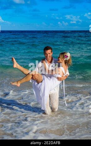 Newly married couple celebrate their wedding on a beach on the Caribbean Island of Mustique. Hand in hand they splash in the surf and trash the dress. Stock Photo