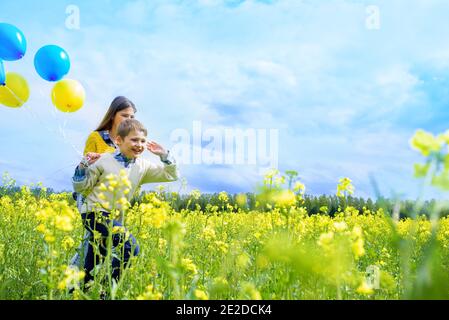 Little happy girl with blue and yellow .Yellow field of rapeseed. happy running kids. concept of freedom, summer. Rapeseed is an alternative energy. Stock Photo