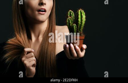 Frustrated woman with long silky straight hair in black body holding cactus plant in pot and comparing with split ends Stock Photo