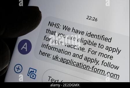 Stafford, United Kingdom - January 13 2021: Scam coronavirus vaccine text message seen on the smartphone screen and blurred silhouette of finger point Stock Photo