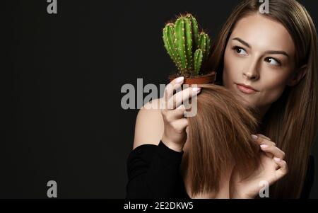 Beauty woman with long silky straight hair compare hair split ends with green cactus plant in pot over dark background Stock Photo