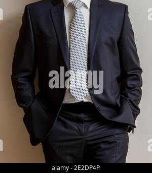 Businessman in a classic black suit with his hands in the pocket leaning on a w Stock Photo