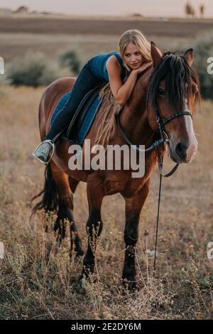 Pretty young girl sitting on horse on nature background. Concept of love, friendship, farm animals