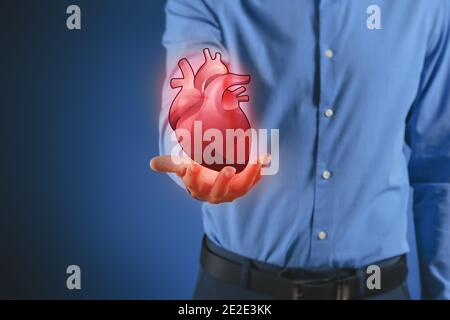 Man with holographic projection of human heart on dark color background. Innovative technologies in medicine Stock Photo