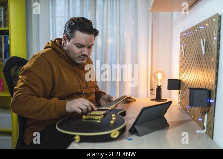 Selective focus shot of a guy with piercings wearing a brown hoodie adjusting a guitar in a room Stock Photo