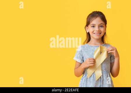 Little girl with golden ribbon on color background. Childhood cancer awareness concept Stock Photo