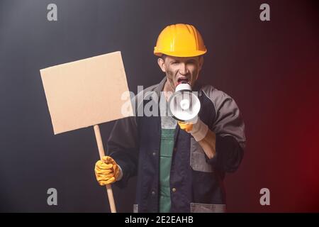 Protesting miner man with megaphone and placard on dark background Stock Photo