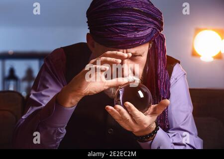 Male fortune teller with crystal ball at home Stock Photo