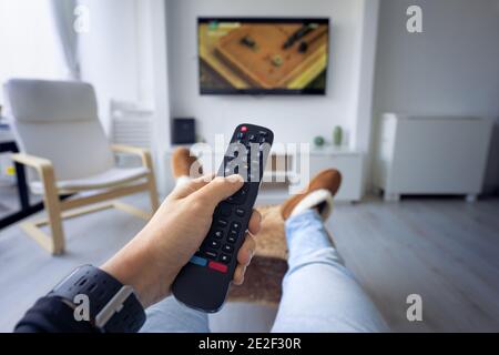 Man watching TV at home. Holding remote controller and switching channel. First person view Stock Photo