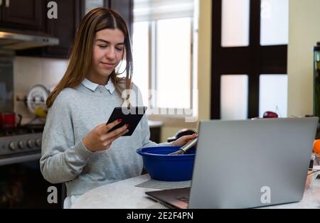 Young woman is using her digital tablet. She is smiling. She is learning to cook with her laptop Stock Photo