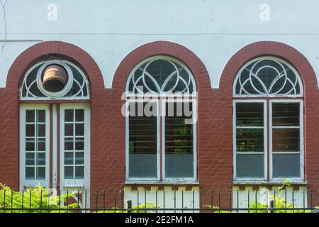 Three old arched windows with wooden frames. Peeled old paint on facade and shutters. Retro window in architecture of last century. Selective focus, b Stock Photo