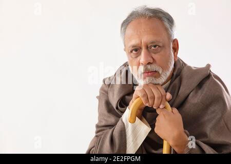 AN OLD MAN HOLDING WALKING STICK SITTING AND LOOKING AT CAMERA Stock Photo