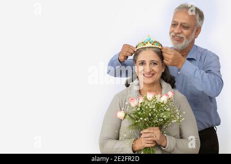 A SENIOR ADULT WOMAN SITTING WITH HUSBAND CROWNING HER HAPPILY Stock Photo